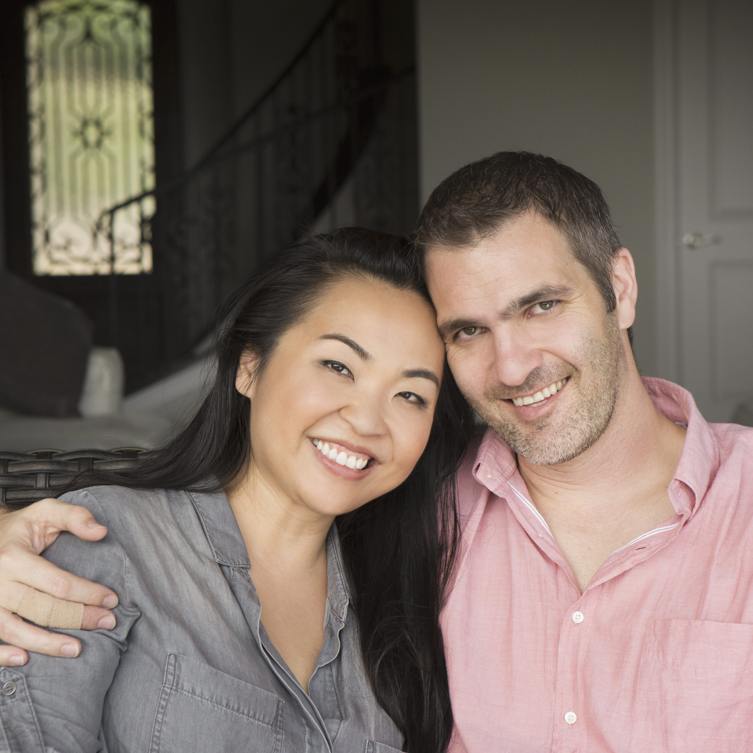 Smiling man and woman sitting on a sofa, hugging, and looking at the camera.